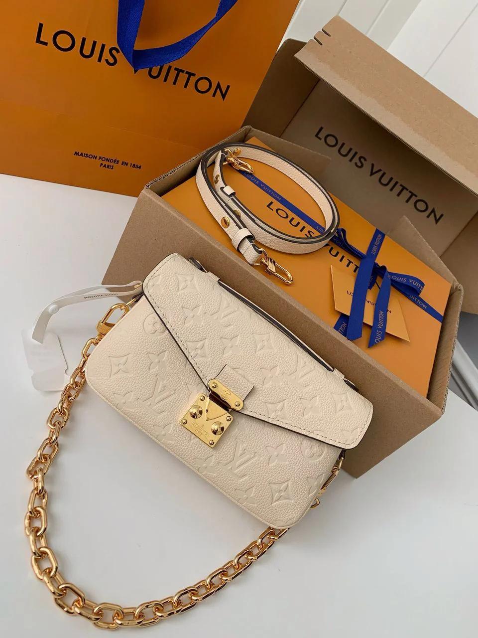 Bolsa marfim monogramada com corrente e alça, caixa aberta, sacola e fita azul.
