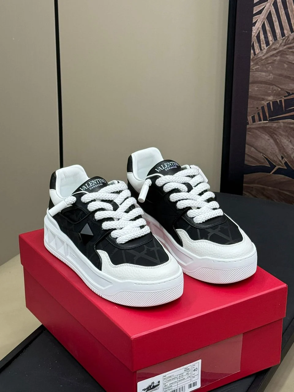 Tênis preto e branco com cadarços grossos sobre caixa vermelha.