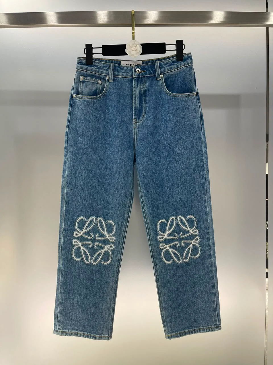 Calça jeans azul com bordados grandes nas pernas, em cabide de pressão.